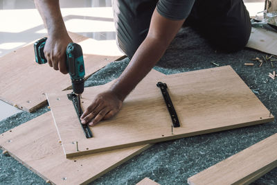 Midsection of carpenter drilling wood in workshop