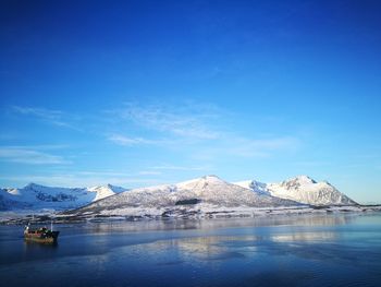 Scenic view of lake and snowcapped mountains against blue sky