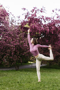 Woman with arm raised practicing yoga in apple blossom garden