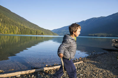 Young boy playing with sticks in nature, lake shore, scenic view.