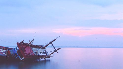 Boat sinking in sea against sky during sunset