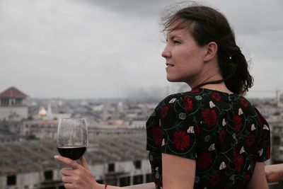 Young woman holding wineglass against sky