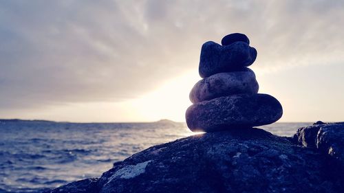 Stack of stones on beach against sky during sunset