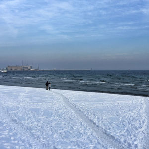 People walking at snow covered beach against sky