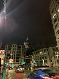 Cars on city street by buildings against sky at night