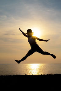 Silhouette of person jumping on beach against sky during sunset