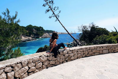 Side view of man on wall by sea against sky