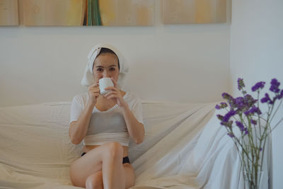 Full length of young woman sitting on bed at home