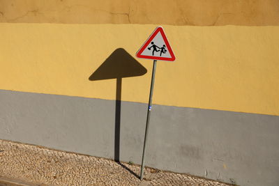 Road sign against wall during sunny day