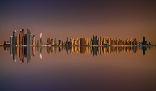 Reflection of buildings on lake against sky during sunset