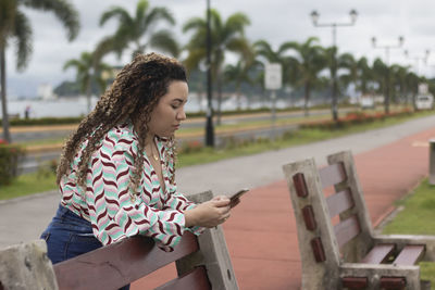 Latin woman with curly hair and cell phone in hand typing	