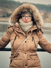 Portrait of woman standing against railing and lake during winter