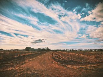 Dirt road amidst field against sky