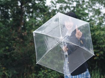 Young woman holding transparent umbrella at park