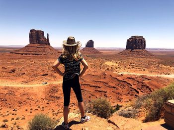 Woman standing on dirt road against blue sky