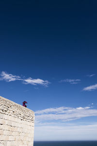 Low angle view of woman on fortified wall against blue sky