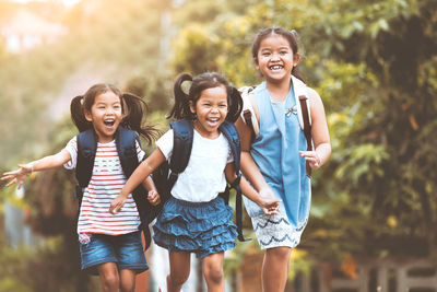 Happy friends running with backpacks against plants