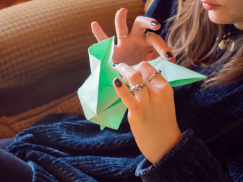 Midsection of woman making paper boat while sitting on sofa at home