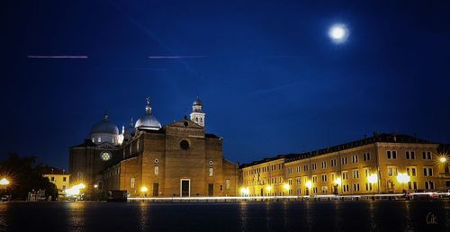 Low angle view of illuminated church by river against sky at night