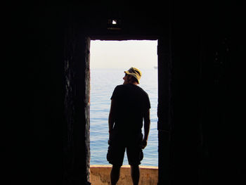 Rear view of mature man standing at doorway against sea