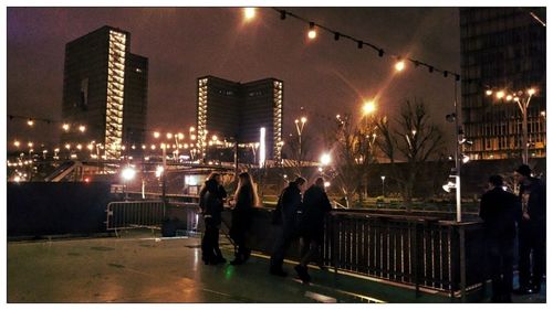 People in illuminated city against sky at night