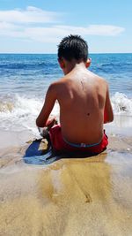 Rear view of shirtless boy on beach against sky