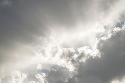 Low angle view of sunlight streaming through clouds