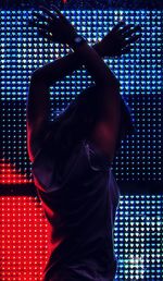 Teenager with arms raised standing by illuminated wall