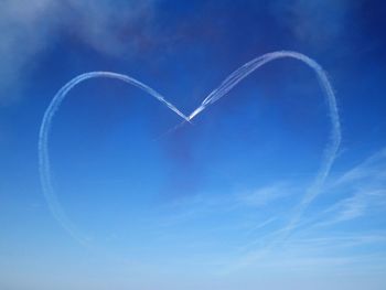 Low angle view of vapor trails forming heart shape in blue sky