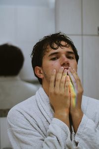 Portrait of young man with hands covering mouth in bathroom