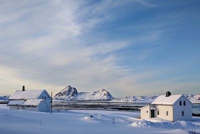 Snow covered houses by building against sky