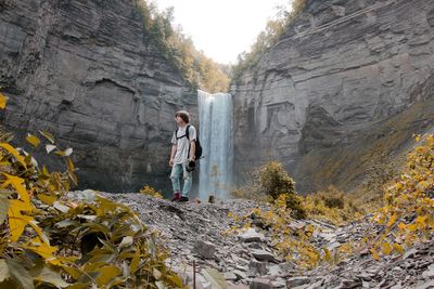 Low angle full length of young man standing against waterfall