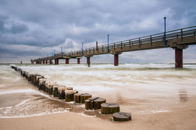 View of pier on beach against cloudy sky