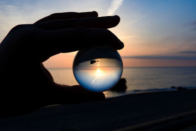 Person holding sun over sea against sky during sunset