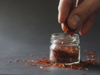 Close-up of human hand removing saffron from bottle on table