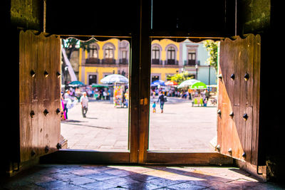 People on city street seen through open wooden window