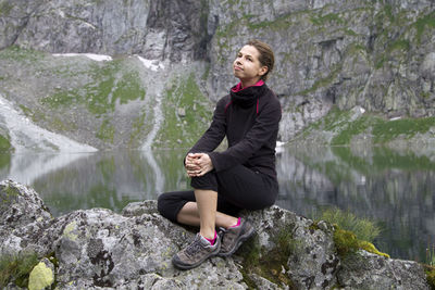 Portrait of young woman sitting on rock by lake