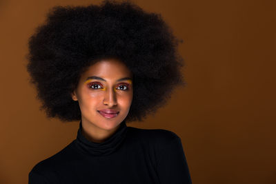 Portrait of beautiful woman with afro hairstyle against brown background