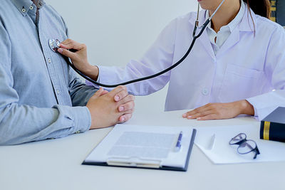 Midsection of female doctor examining patient with stethoscope