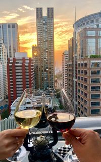 Cropped hands toasting wineglasses at table against buildings