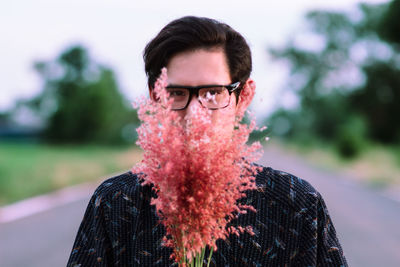 Portrait of man with coral flowers standing on road