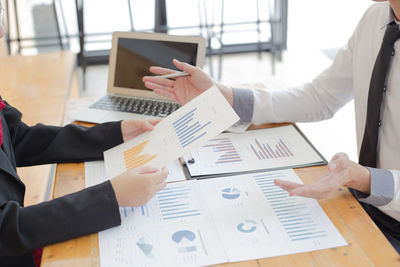 Cropped image of business colleagues analyzing graph on desk in office