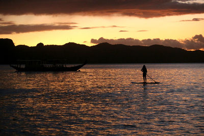 Silhouette man in sea against sky during sunset