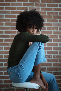 Beautiful black woman with afro hair sitting on the chair against the brick wall background
