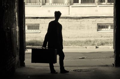 Silhouette boy with suitcase walking on road in city