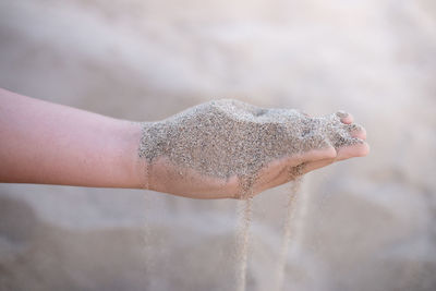 Sand puffs through the fingers of a girl's hand.