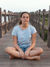 Teenager sitting cross legged on the wooden walkway by the sea 