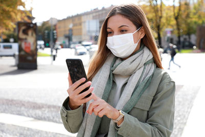 Young woman wearing mask using mobile phone on street