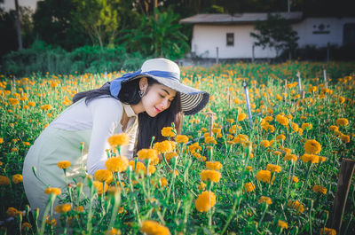 Young woman wearing hat while smelling flowers on field