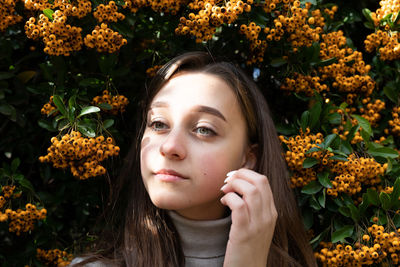 Close-up of thoughtful young woman standing against orange berries on plant